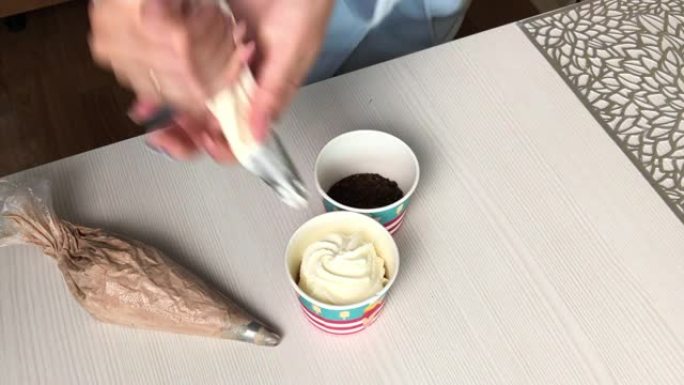 一个女人用奶油和饼干屑做冰淇淋。将糕点袋中的奶油放在碗中的饼干屑上。