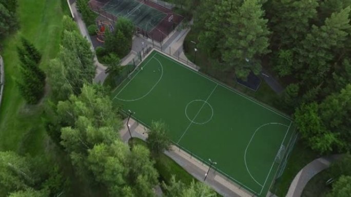 足球场和篮球场的鸟瞰图。孩子们在踢足球。树木环绕的运动场。阳光眩光。公园区