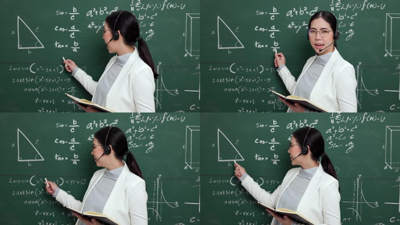 年轻的亚洲女教师拿着粉笔戴着耳机视频会议，配有学生摄像机。女教师培训课堂黑板在线课程中的数学。