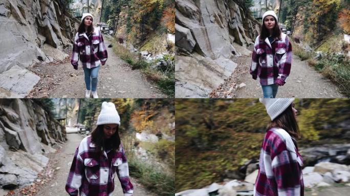 一个女孩正穿着女孩的衬衫和帽子走在山中。凉爽的天气