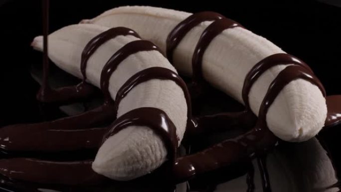 将两个新鲜的去皮香蕉倒在黑色盘子上，并倒入热液体巧克力。