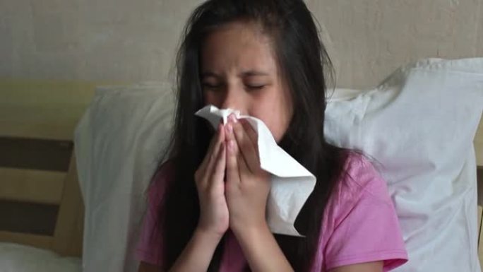 一个穿着粉红色t恤的黑发可爱的女孩坐在床上，生病，吹鼻子，用毛巾餐巾擦拭鼻子上的鼻涕