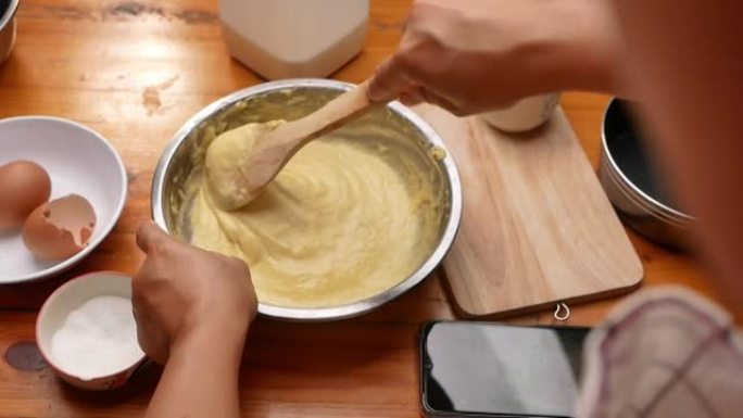 雌性手将面粉，新鲜牛奶和鸡蛋与刮铲混合，为自制玉米棒准备面糊。烹饪过程。