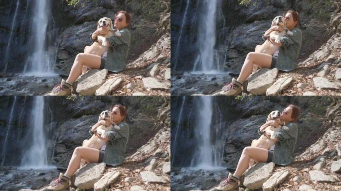4k女人坐在瀑布附近的户外拥抱她的小猎犬