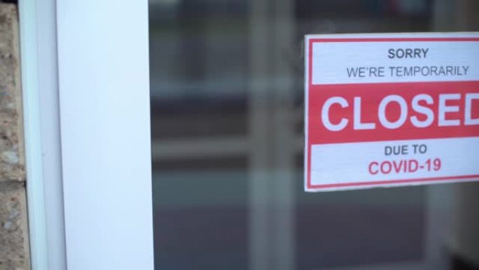 在新型冠状病毒肺炎大流行期间，一名男子在透明的门或店面上悬挂着一个封闭的标志