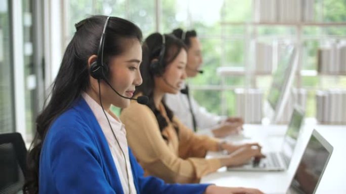 美丽的亚洲女性呼叫中心代理在她的工作站上与客户交谈