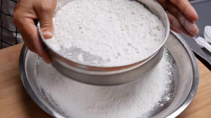 女性双手用面粉过滤器将面粉筛入不锈钢容器中，制成面团，制成美味的自制披萨。烹饪过程。