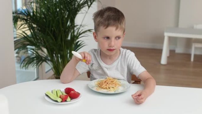 厨房里的男孩在家里吃意大利面时微笑着。好孩子食欲概念