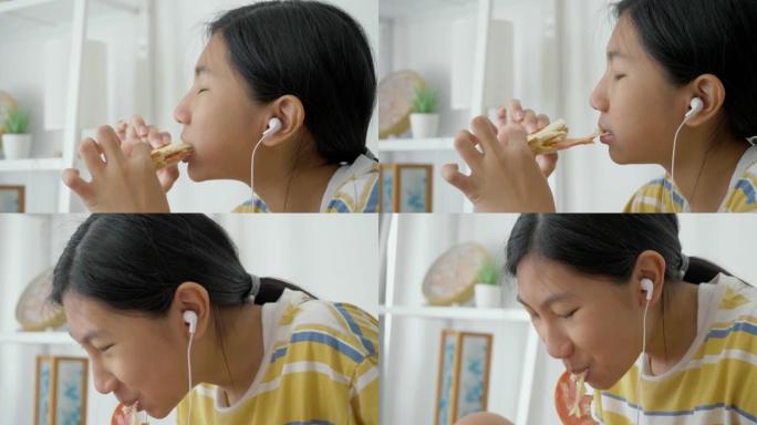 亚洲女孩吃火腿烤面包，并在看智能手机电影时，生活方式概念。