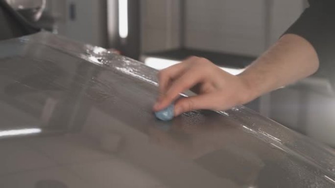 在将保护层或PPF涂层安装到汽车上之前，工人用蓝色粘土清洁车身以进行清洁。汽车细节概念