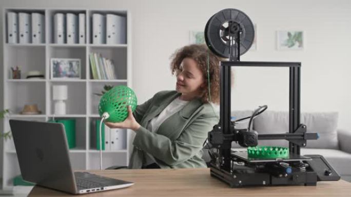 家装，女设计师，手中的3D打印打印机上的灯罩3D模型原型在家，微笑着看着相机