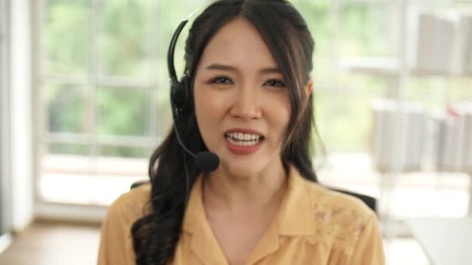戴着耳机和支持客户，看着相机工作的亚洲女性呼叫中心的肖像照片