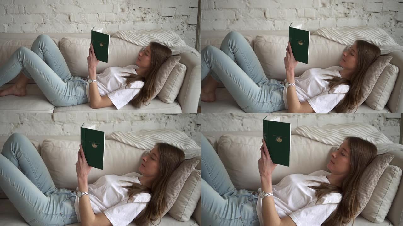 宁静的女人在家躺在沙发上看纸质书