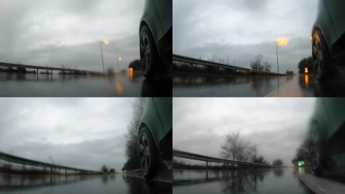 详细说明汽车后轮在潮湿的道路上在大雨中行驶。雨水溅到相机上