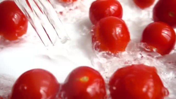 将红樱桃番茄倒入水中。洗西红柿。在白色背景上。慢动作。