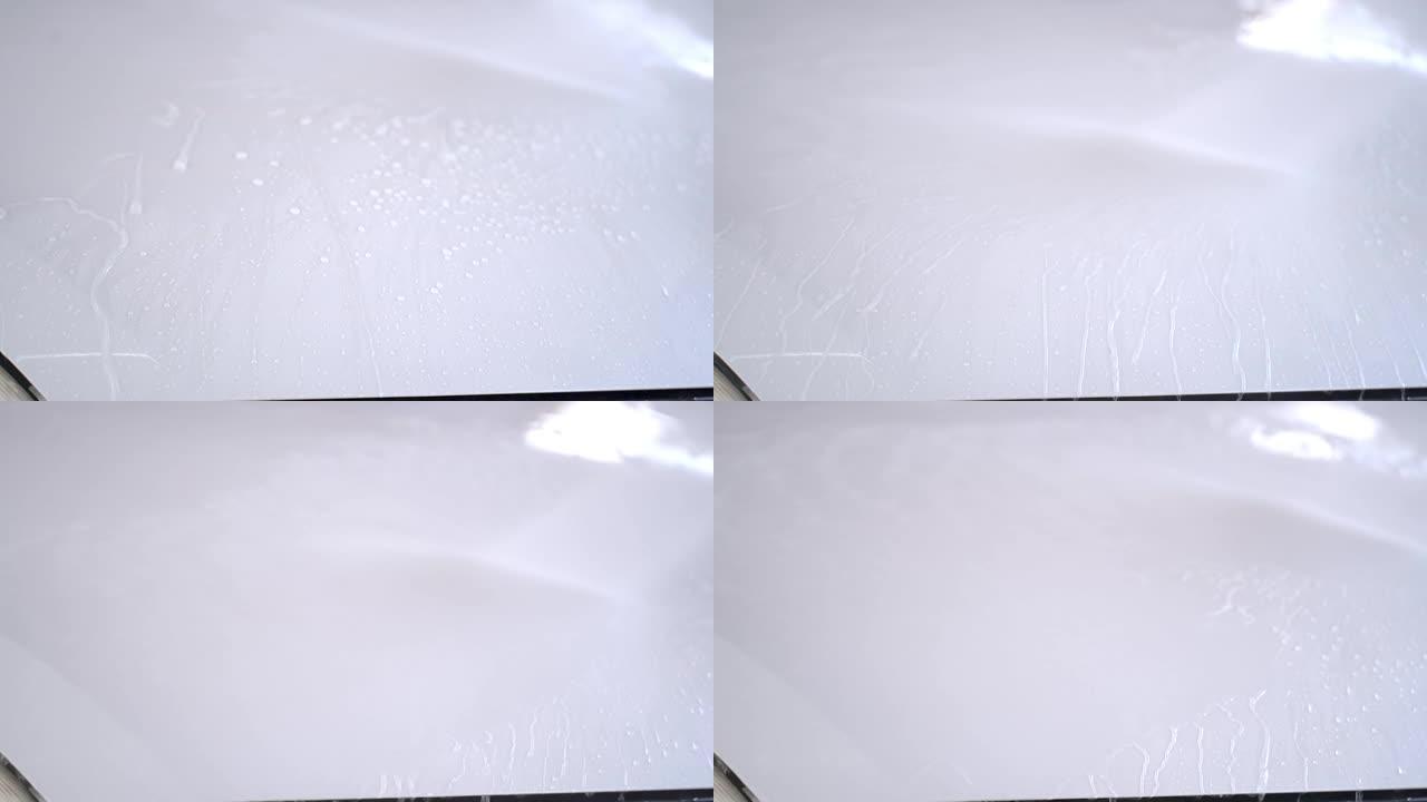 水雾清洗一辆白色汽车。关闭车库部分车辆侧门和前玻璃的喷水清洗。在车辆上使用喷水喷雾的工人。