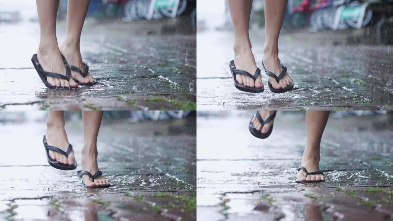 在季风引起的雨天，人字拖中的低角度镜头脚踩在水坑上，喜欢在铺路人行道周围跳跃和飞溅水滴，慢动作，热带