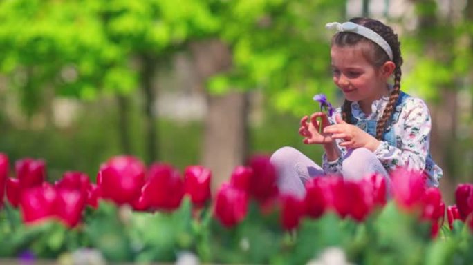 美丽的小女孩享受春天郁金香和彩色花朵的彩色花园