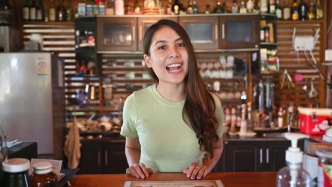 年轻的亚洲女性收银员在咖啡店的木制柜台与顾客打招呼