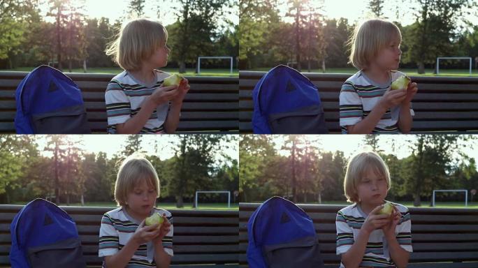 小学生背着背包坐在学校院子附近的长凳上，放学后或课间休息时吃苹果作为零食