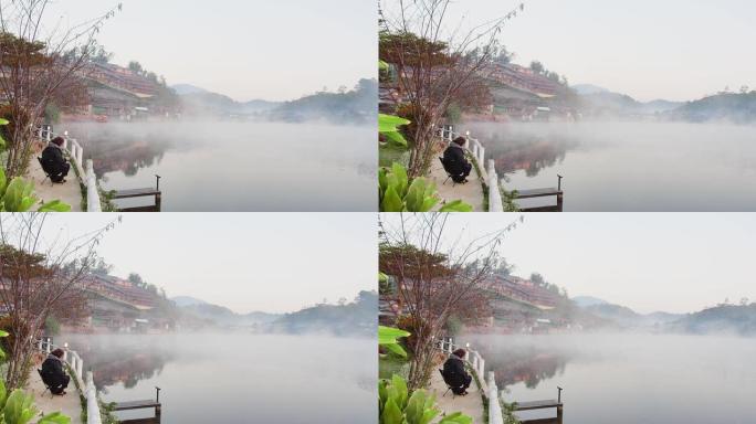大自然中的美丽晨景和旅游妇女坐在河边放松，湖雾迷雾和中国风格的乡村山在泰国湄宏顺班拉克泰国村的背景下