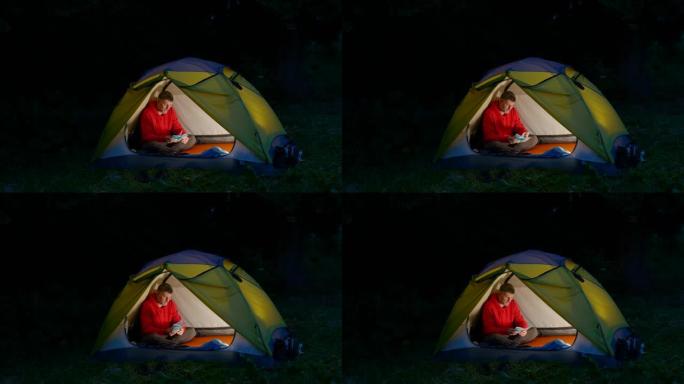一个男人在夜林里的帐篷里翻阅笔记本