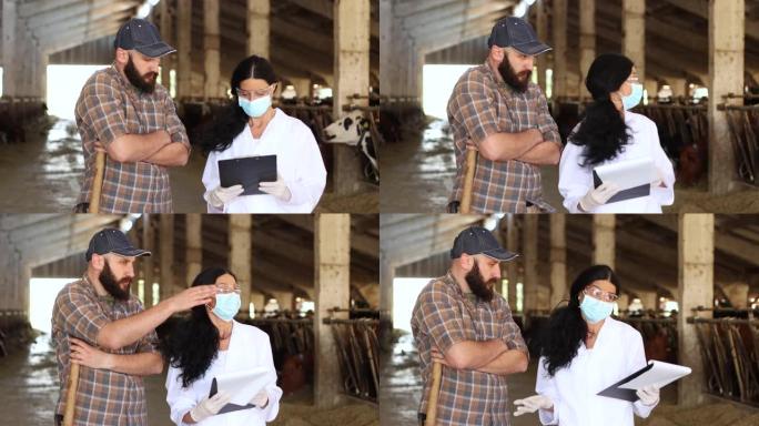 一名身穿白色工作服、戴着防护面罩的女专业人员，用手指着不同的方向，在一个大型牛场与一名男农民交谈。