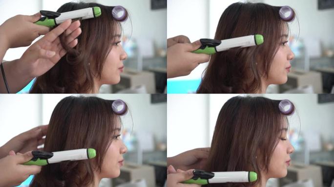 年轻的发型师为亚洲女性客户提供卷发棒(中国、日本、韩国或泰国)。隔离结束了