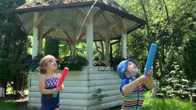 可爱的快乐的孩子，学龄前的小女孩和男孩的孩子玩有乐趣的水泵枪在外面。阳光明媚，公园里的一天。儿童后院