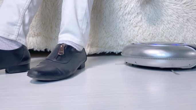 白色木地板上的机器人吸尘器和沙发上的快乐女仆的腿。智能家居概念。