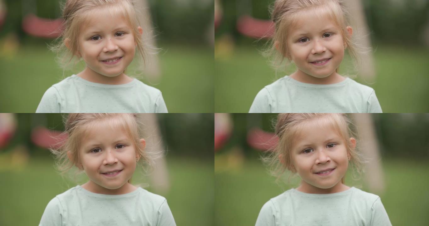 可爱的金发孩子，天真的眼睛胆怯，看着相机，在后院外面玩耍时微笑着