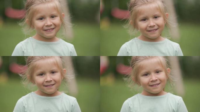 可爱的金发孩子，天真的眼睛胆怯，看着相机，在后院外面玩耍时微笑着
