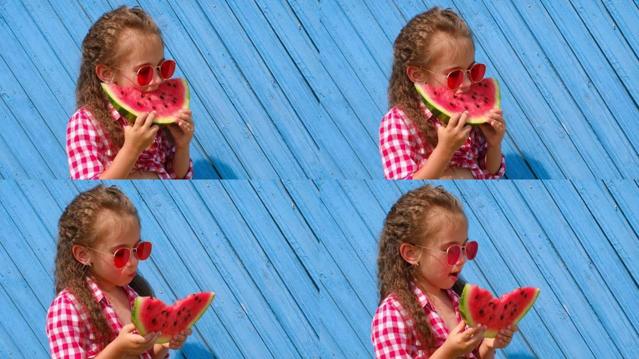 一个戴着红色太阳镜的漂亮可爱的女孩吃一块甜美多汁的西瓜，舔她的嘴唇。全国西瓜日。