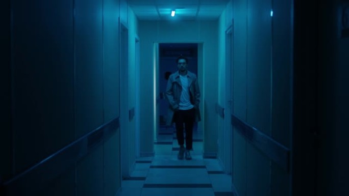穿着外套的男人沿着医院的深蓝色走廊走