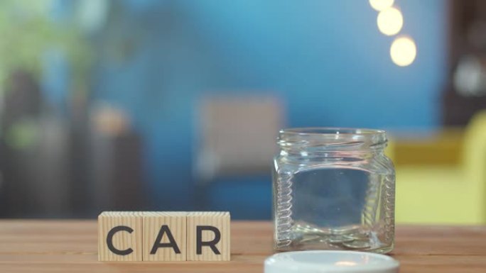 汽车是写在桌子上的木制立方体上的单词。手把钱放在附近的罐子里。积累大量资金进行大额购买的概念