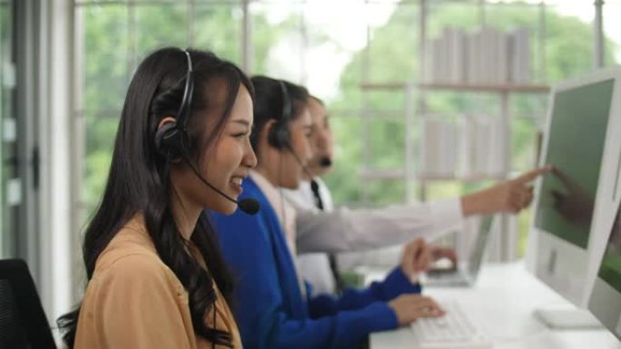 亚洲女性呼叫中心代理在其工作站上与客户交谈