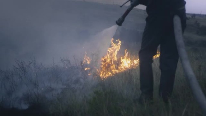 一名消防员手里拿着一根装有水的软管，扑灭了燃烧的火焰。大自然着火了: 草，草原，森林和田野