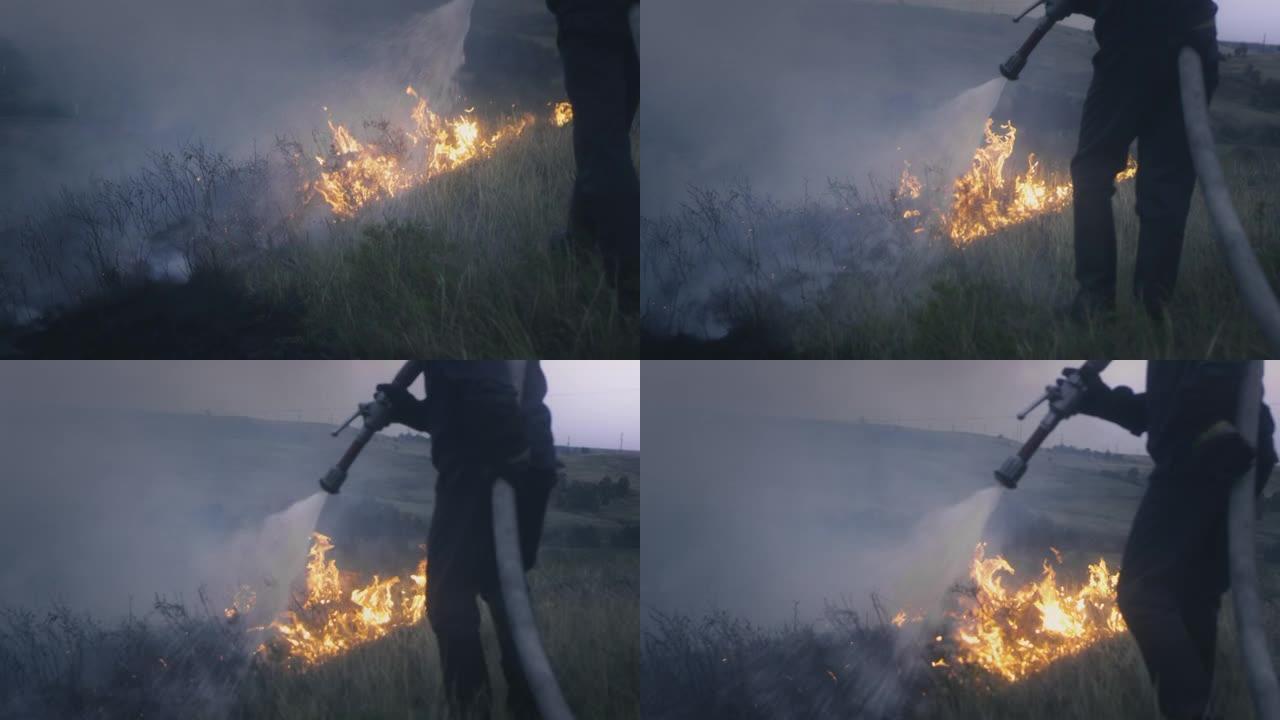 一名消防员手里拿着一根装有水的软管，扑灭了燃烧的火焰。大自然着火了: 草，草原，森林和田野