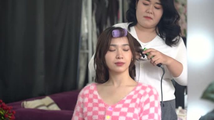 年轻的发型师为亚洲女性客户提供卷发棒(中国、日本、韩国或泰国)。隔离结束了