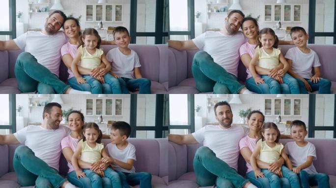 西班牙裔妇女有两个混血孩子，坐在沙发上靠近丈夫，把头靠在头上，对镜头微笑。4k快乐多种族家庭视频肖像