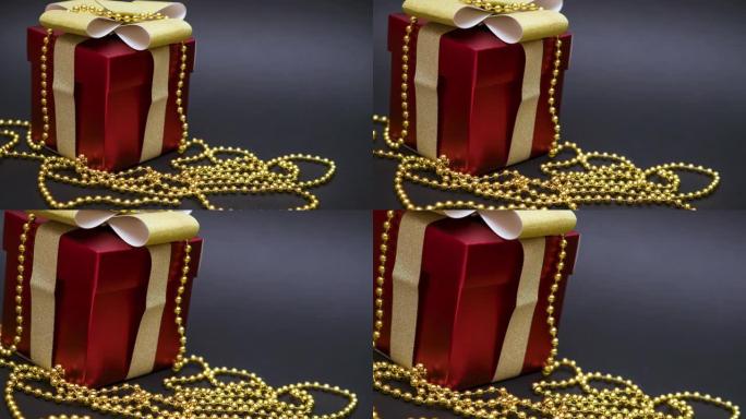 美丽的红色礼品盒，黑色背景上有金色蝴蝶结和珠子。