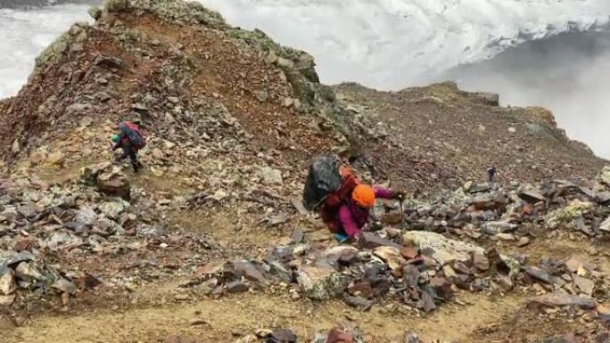 一个背着大背包的疲倦游客沿着山间小路跌跌撞撞地走过石头和巨石