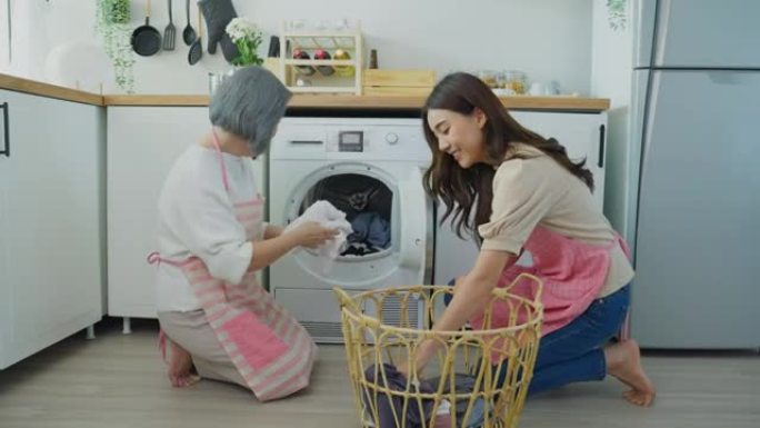 亚洲可爱的家庭在家做家务和家务。年轻的女孩女儿帮助和支持资深的老母亲把衣服放在洗衣机里洗衣服。内务和