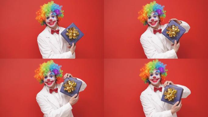 有趣的小丑手里拿着一个礼品盒，在孤立的红色背景下为相机摆姿势