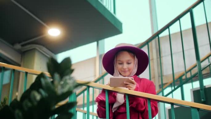可爱的微笑女孩站在楼梯上使用智能手机