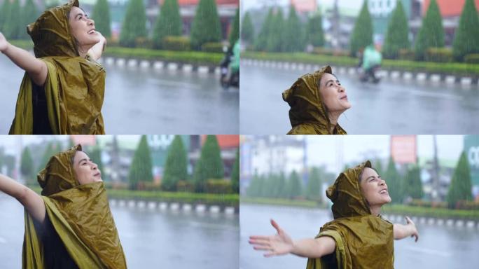 在倾盆大雨的日子里，一个脸上表情积极的亚洲女孩，穿着黄色的雨衣站在路边，在雨中浸湿了，这是亚洲的雨季