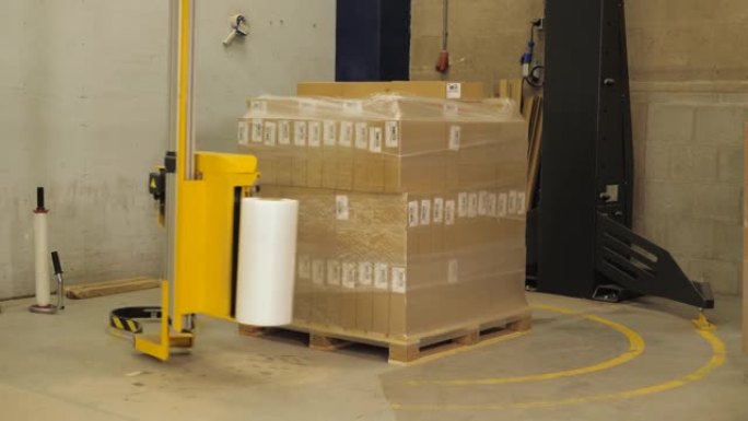 机器在工厂用纸板箱将塑料包裹在托盘上