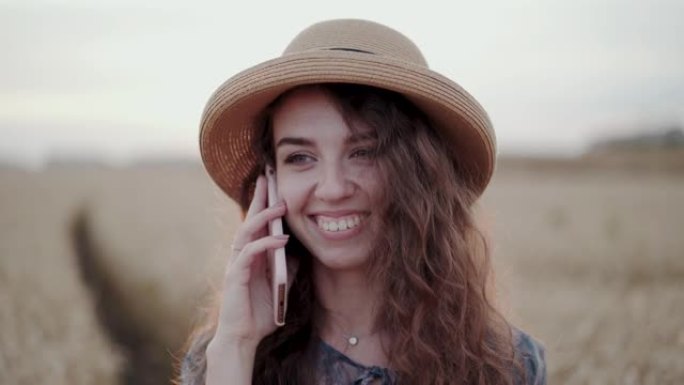 一幅戴着帽子的美丽女士在麦堆里微笑着打电话的画像