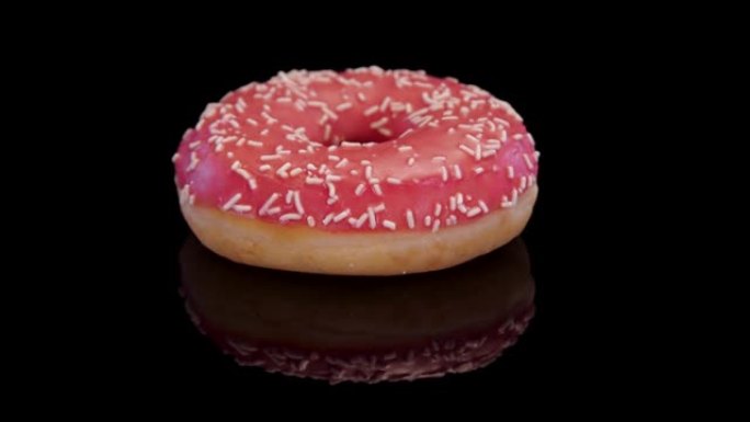 在黑色背景上撒上粉红色糖霜和糖的甜甜圈。甜甜甜圈，结霜，撒上隔离。概念: 甜食，面包店，垃圾食品