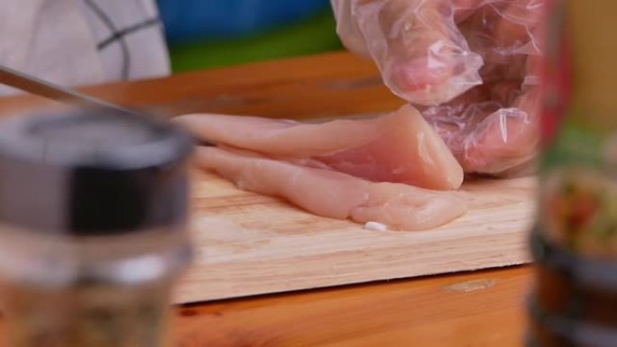 戴着手套的女人正在木制砧板上切鸡肉，准备好吃的食物。自制烹饪概念。